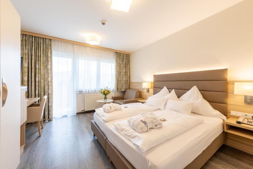 Hotel Grimmingblick room with large bed, white linens, and natural light from balcony doors.