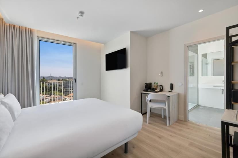 Modern hotel room with white bedding, desk, TV, and balcony view of Porto Centro Massarelos.