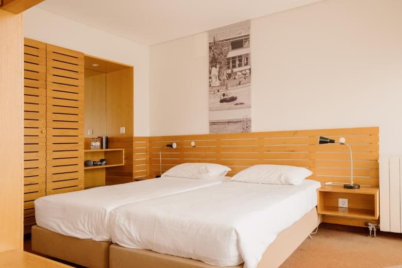 Twin beds with white linens in a modern hotel room featuring light wood paneling and built-in storage.