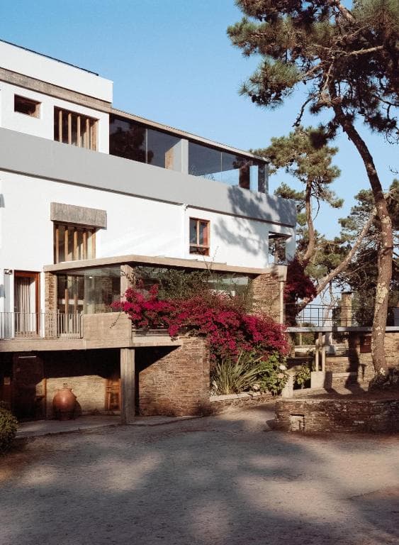 Modern white building with stone accents, red bougainvillea, and pine trees in Esposende.