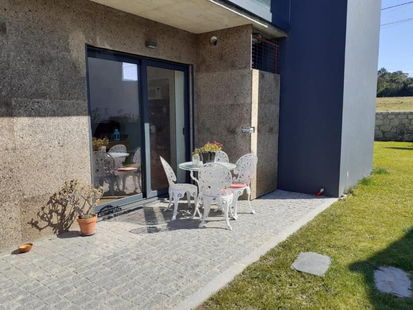 White wrought iron patio set on stone patio next to modern house and green lawn