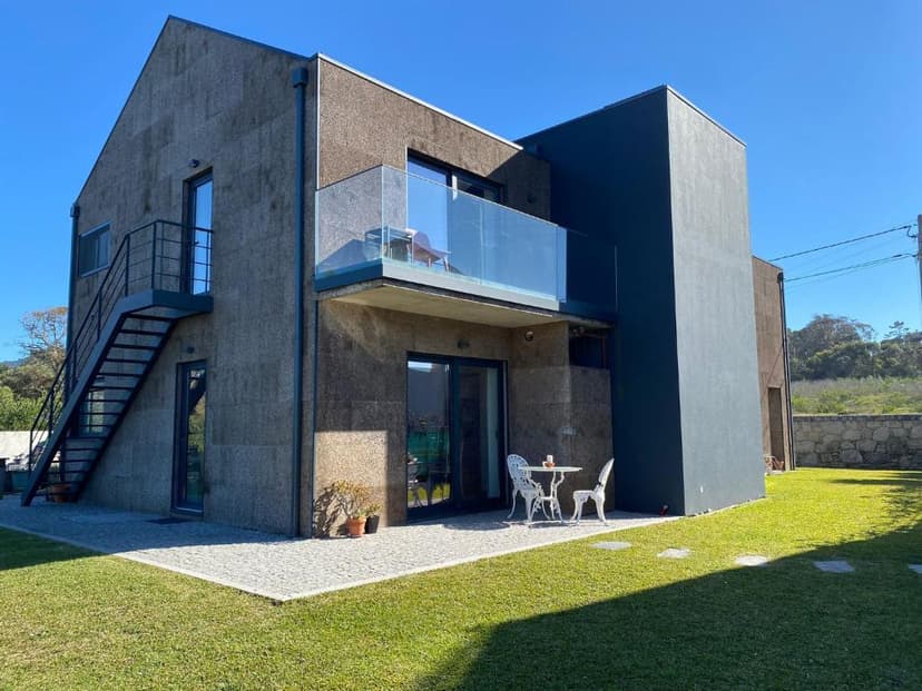 Modern house with cork exterior, metal staircase, and patio furniture on a sunny lawn.