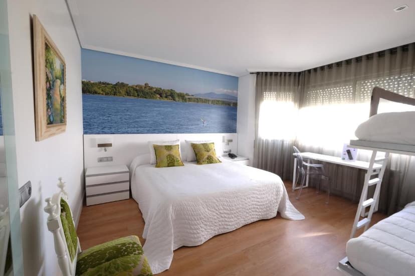 Hotel room with white bedding, green accent chair, and mural of a wide river and bridge.