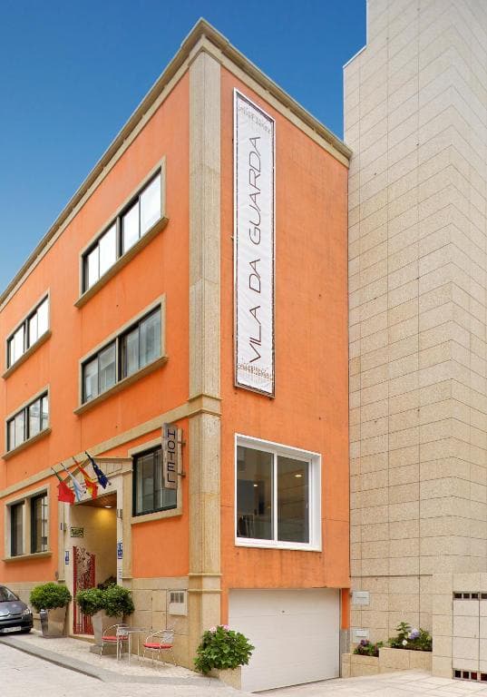 Hotel Vila da Guarda exterior with orange facade and vertical banner under clear blue sky.