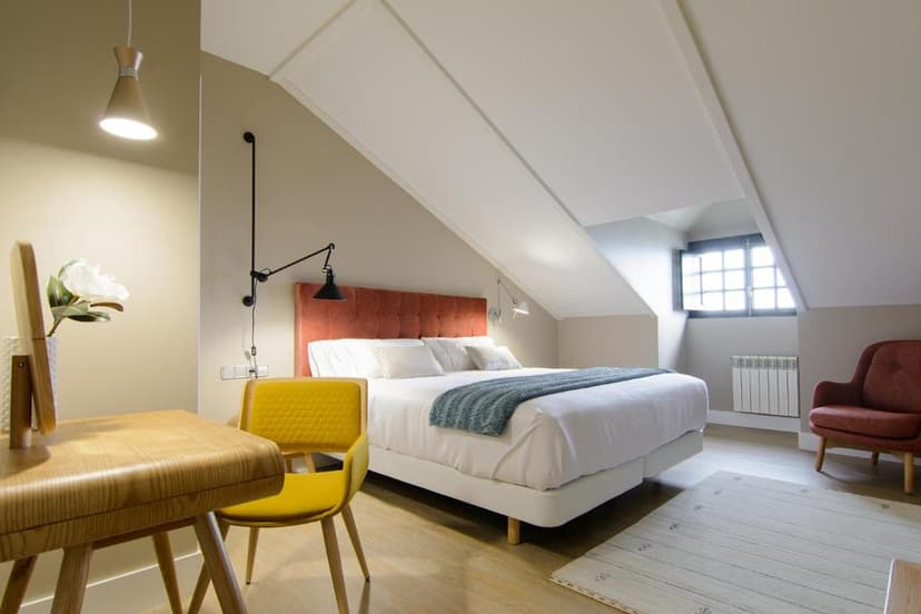 Attic hotel bedroom with white bedding, orange headboard, yellow chair, and sloped ceiling.