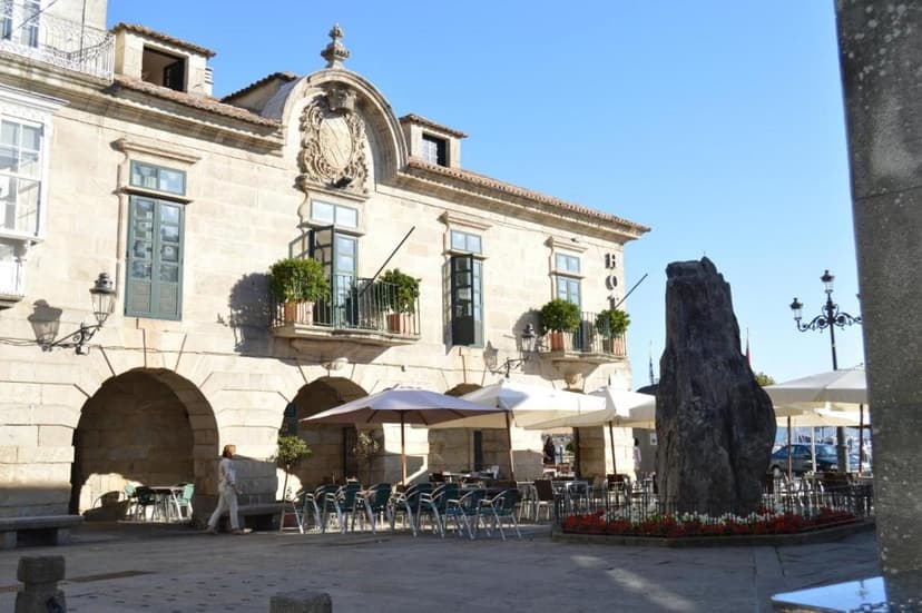 Historic stone building with balconies in Pazo de Mendoza square with outdoor cafe seating.