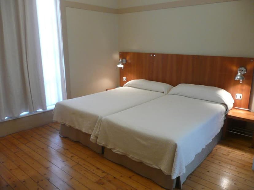Twin beds with white linens in a hotel room with wood floors and a bright window.