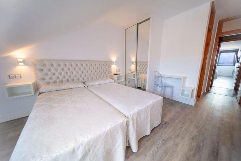 Twin beds with tufted headboard in bright white hotel room with wood floor.