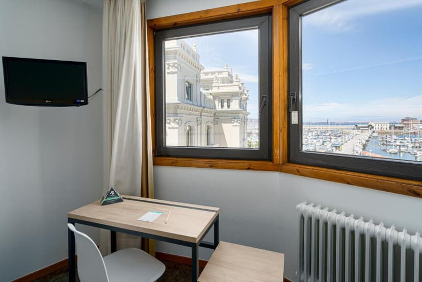 Hotel room with desk, TV, and view of ornate building and marina.