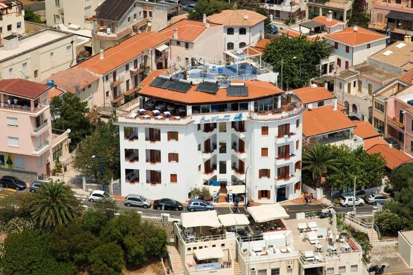 White hotel building with terracotta roof surrounded by other buildings and palm trees in a coastal town.