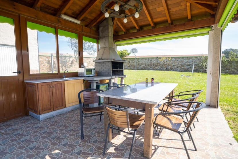Outdoor covered patio with built-in grill, dining table, and view of grassy yard.