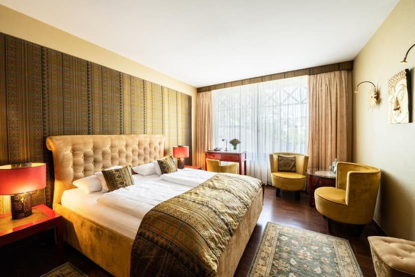Hotel room with tufted gold bed, patterned wall, and yellow velvet chairs near window
