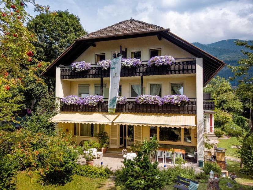 Alpine Bio Hotel with balconies full of purple flowers and outdoor patio seating in Bavaria.