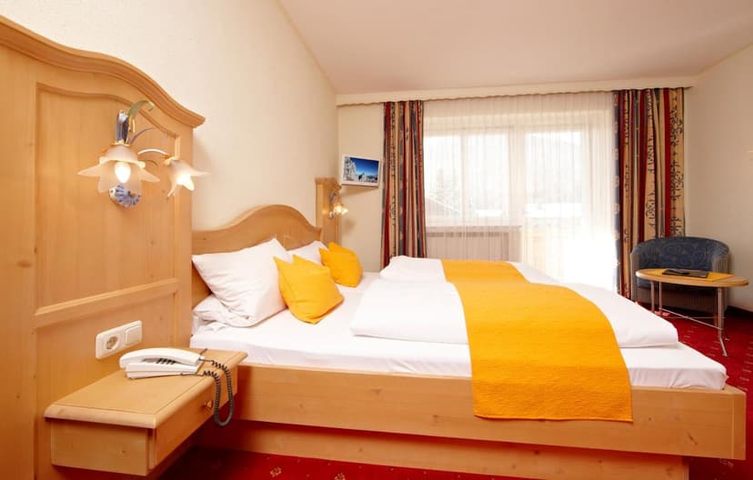 Alpenhotel Rieger room with wooden bed, white linens, orange runner, and bright window view.