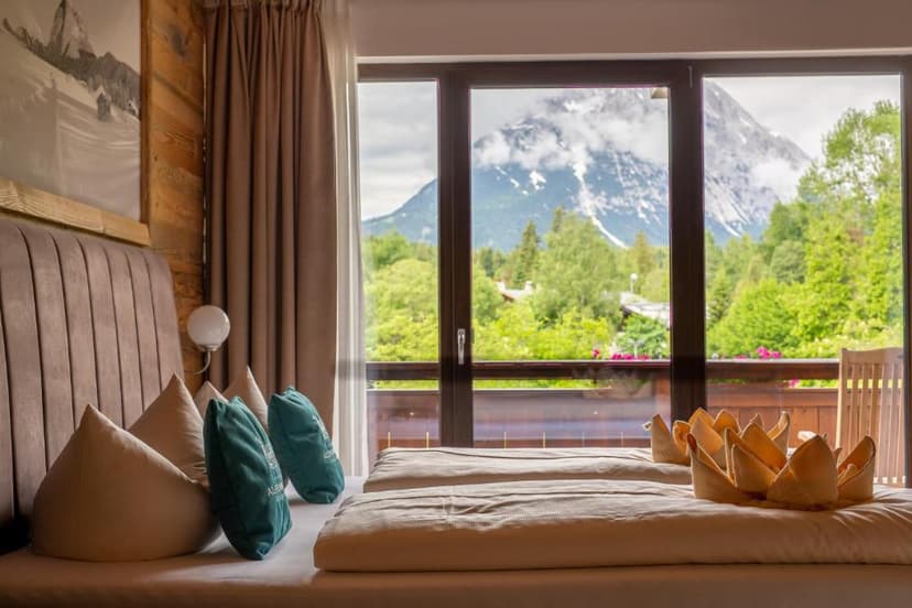 Hotel room with twin beds and balcony view of lush green mountains with snow patches
