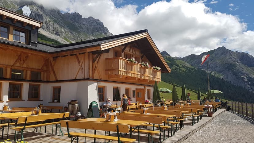 Outdoor dining at Hochfeldern Alm with wooden tables against a backdrop of steep green and rocky mountains.