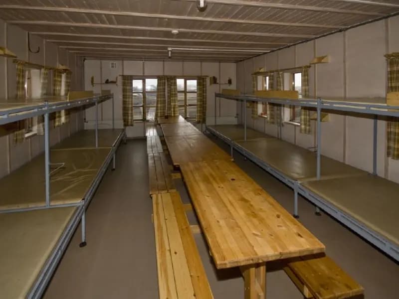 Interior of Hrafntinnusker mountain hut with long wooden tables and metal bunk beds.