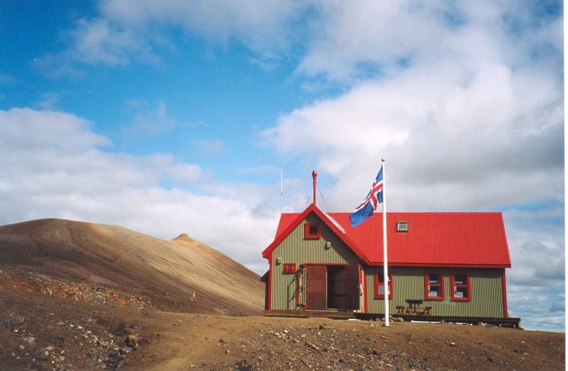 Hrafntinnusker mountain hut with Icelandic flag flying, set against barren hills and blue sky.