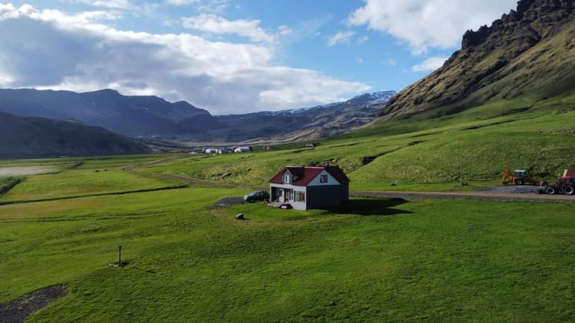 Guesthouse Rauðafell in a green valley with mountains and blue sky.