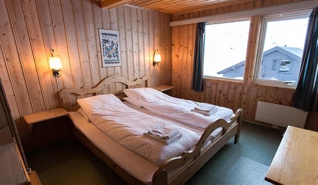 Twin beds with white duvets in a wood-paneled room overlooking a snowy exterior at Leirvassbu.