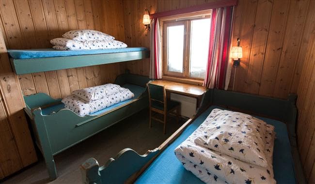 Simple wooden cabin room with bunk beds, single bed, and window at Leirvassbu.