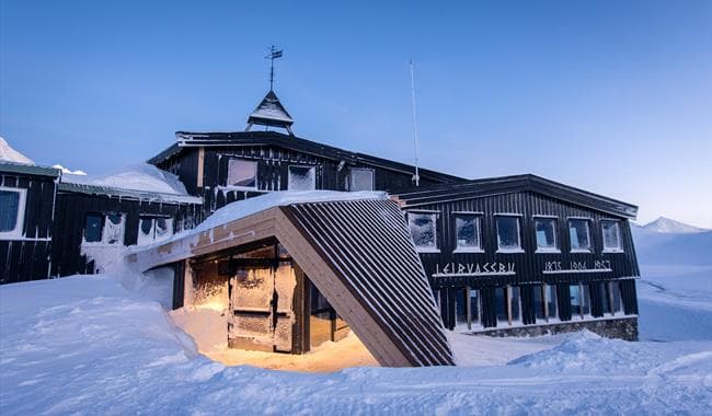 Leirvassbu mountain lodge heavily covered in snow under a clear blue winter sky.