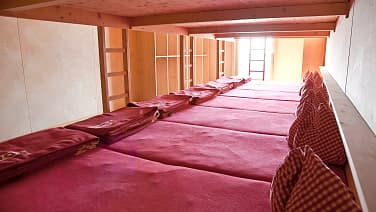 Wooden bunk room interior with long row of red sleeping mats and pillows at Stüdlhütte.
