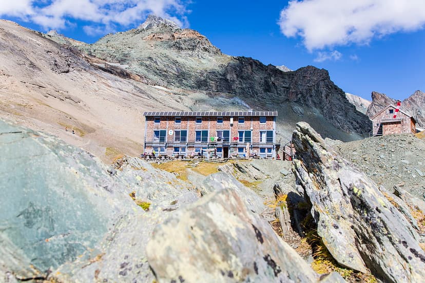 Stüdlhütte mountain hut below rocky peaks on sunny day, foreground rocks.