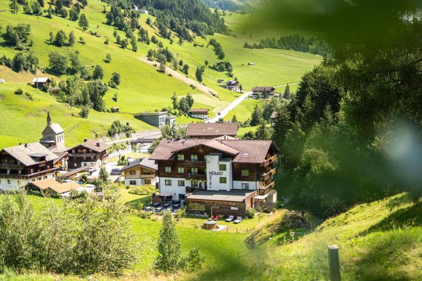 Hotel Heimat in a green alpine valley village with traditional wooden buildings and steep grassy slopes.