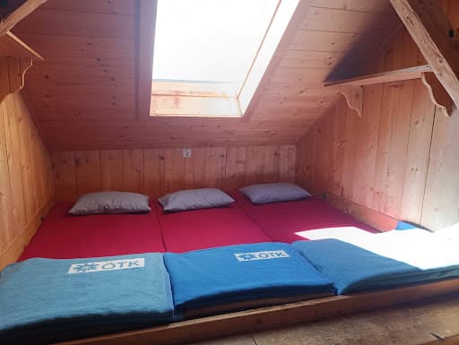 Wooden attic sleeping area with three mattresses, pillows, and blue blankets marked ÖTK.