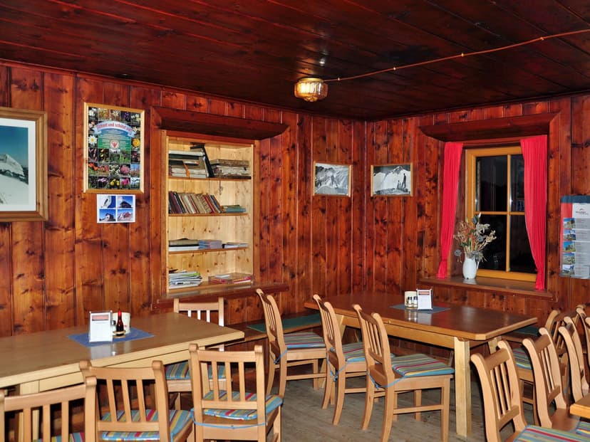 Interior dining room with wood paneling, wooden tables, chairs with striped cushions, and mountain photos.