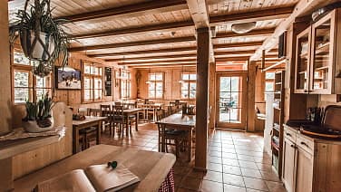 Rustic wooden interior of a mountain hut or restaurant with tables and chairs.