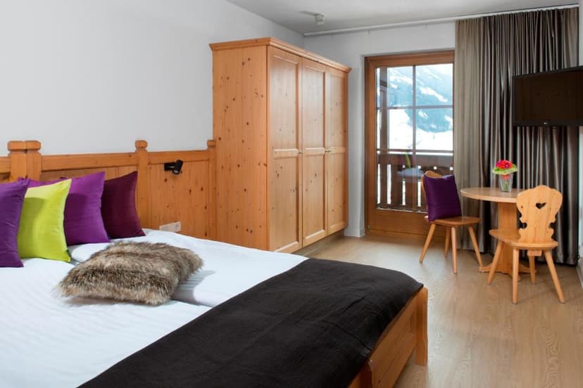 Hotel room with wooden furniture, colorful pillows, and balcony view of snowy mountains.