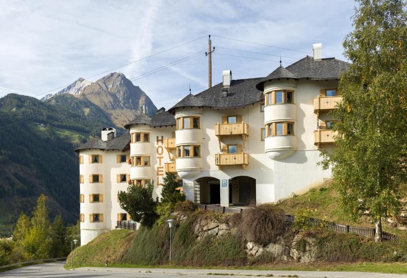Hotel Goldried building with turret windows nestled on a grassy slope against large mountains.