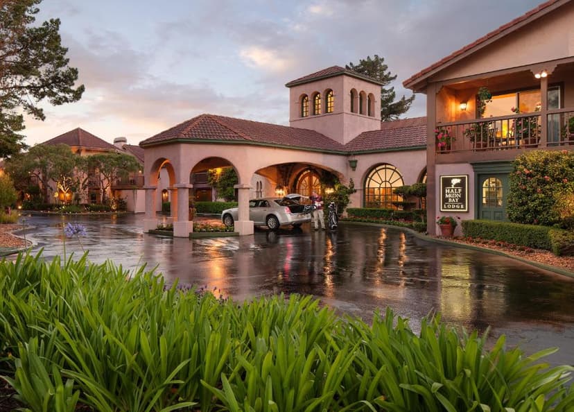 Half Moon Bay Lodge entrance with wet driveway and person loading golf clubs at dusk