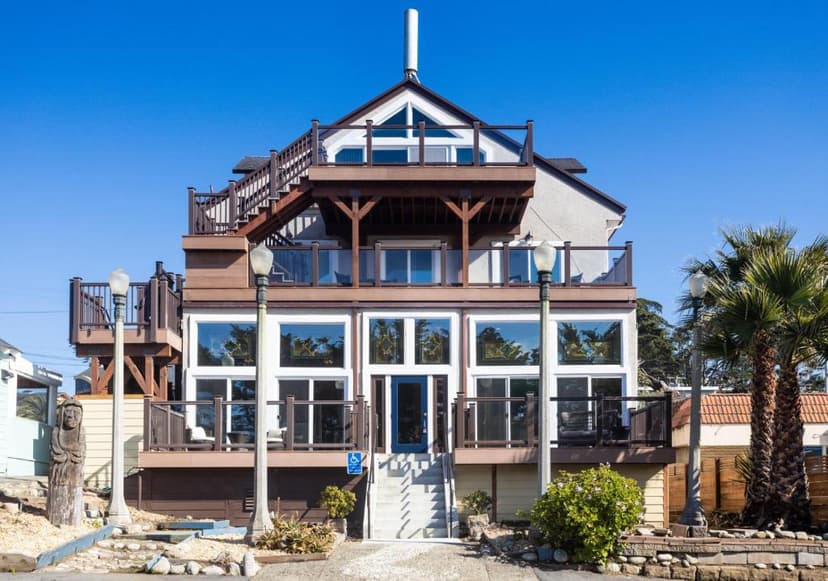 Ocean View Inn with multiple wooden decks, large windows, and palm trees under a clear blue sky.