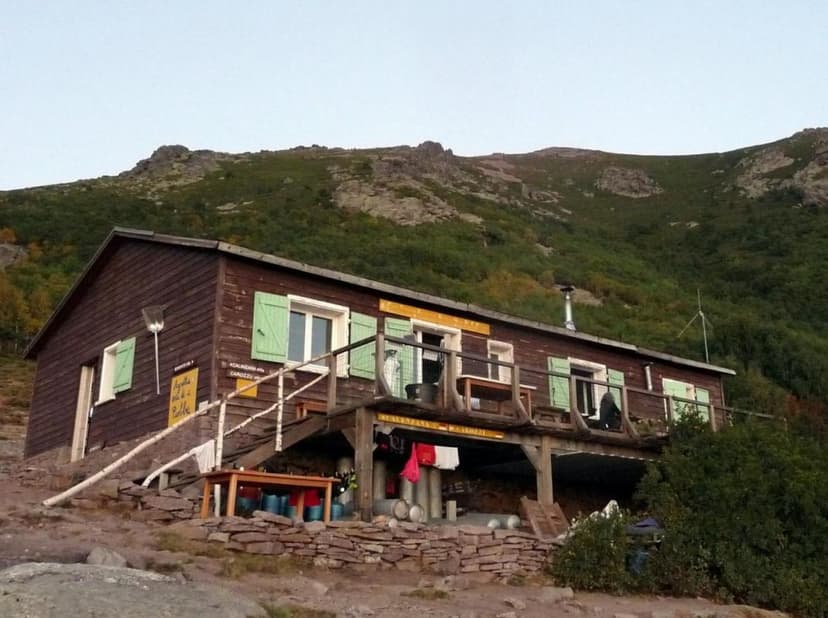 Refuge d'Ortu di u Piobbu wooden mountain hut with green shutters against a steep, scrub-covered slope.