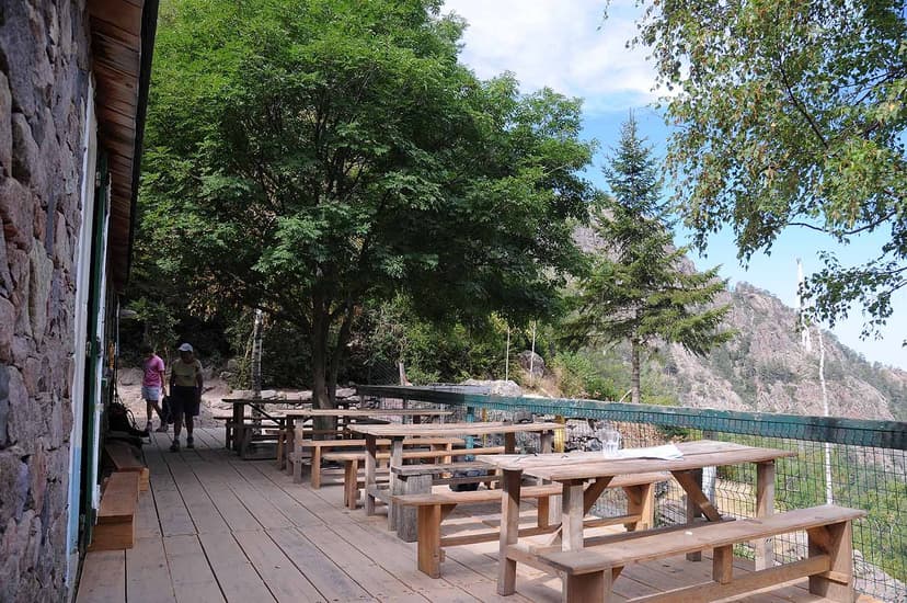 Wooden terrace with picnic tables outside stone building near mountains at Refuge de Carrozzu