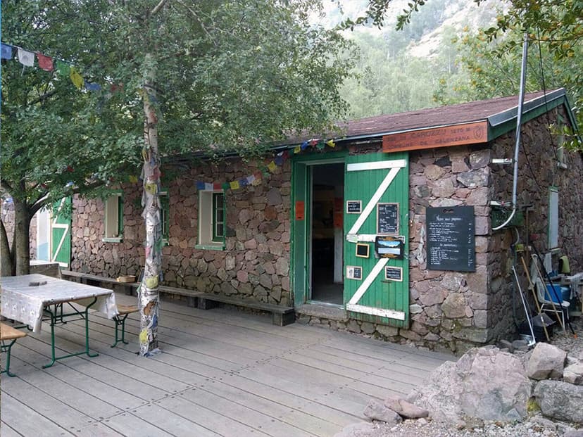 Refuge de Carrozzu stone hut with green door, wooden deck, and prayer flags in the mountains.