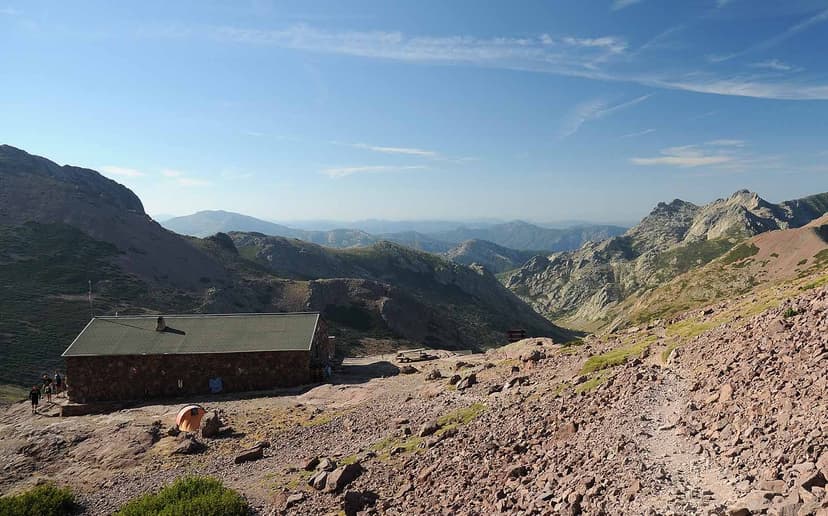 Refuge de Ciottulu di i Mori stone hut in rocky mountain landscape under blue sky.
