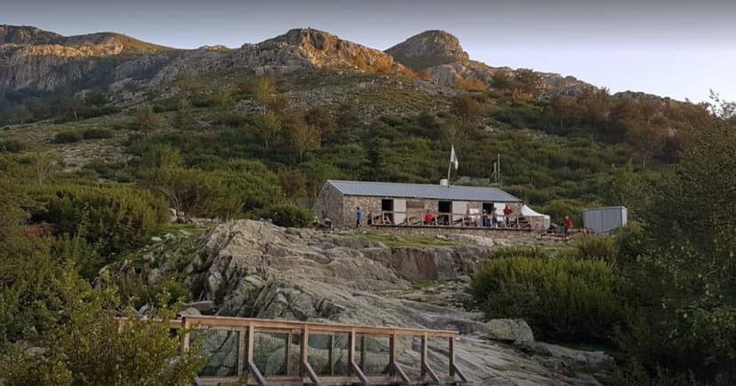 Refuge de Manganu stone mountain hut with people on the terrace below rocky peaks.