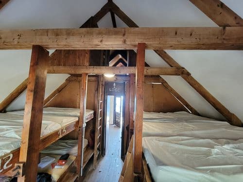 Bunk beds in a rustic attic dormitory with exposed wooden beams at Refuge de Pietra Piana.