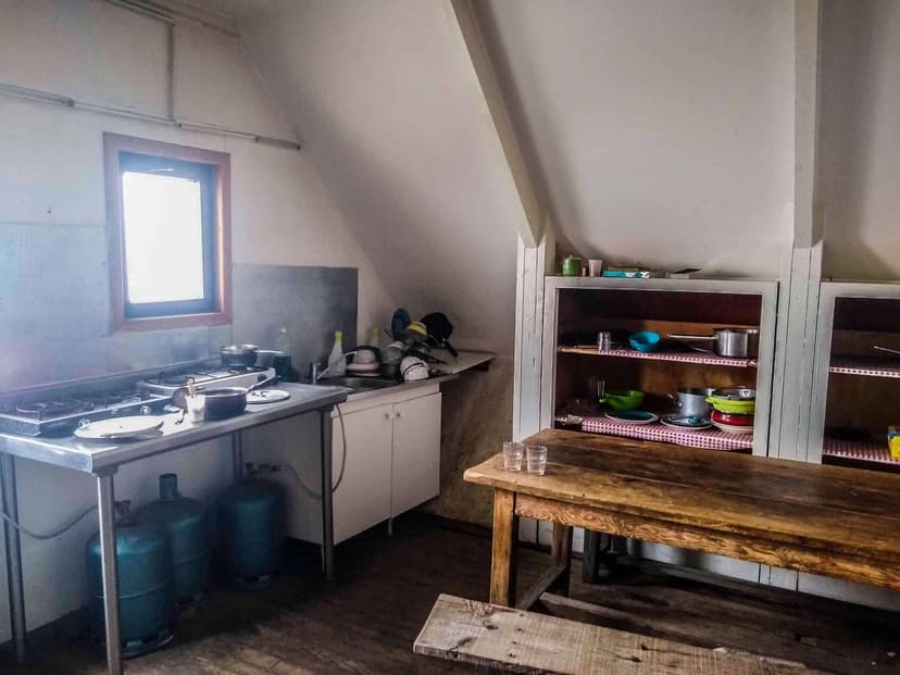 Rustic communal kitchen with stainless steel counter, gas tanks, and wooden table at Refuge de Pietra Piana.