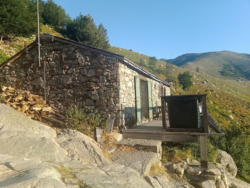 Stone refuge hut with wooden deck on steep hillside near Refuge de l'Onda, Corsica.