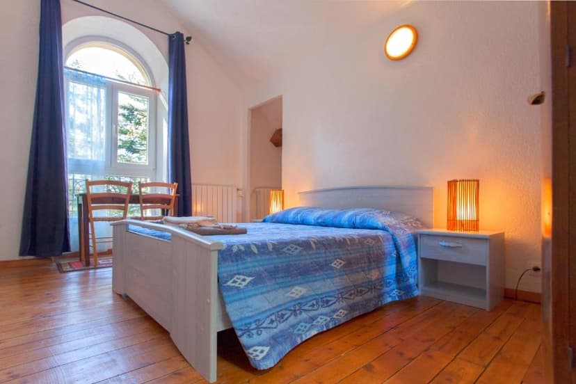 Bedroom with white walls, wooden floor, and arched window with blue curtains.