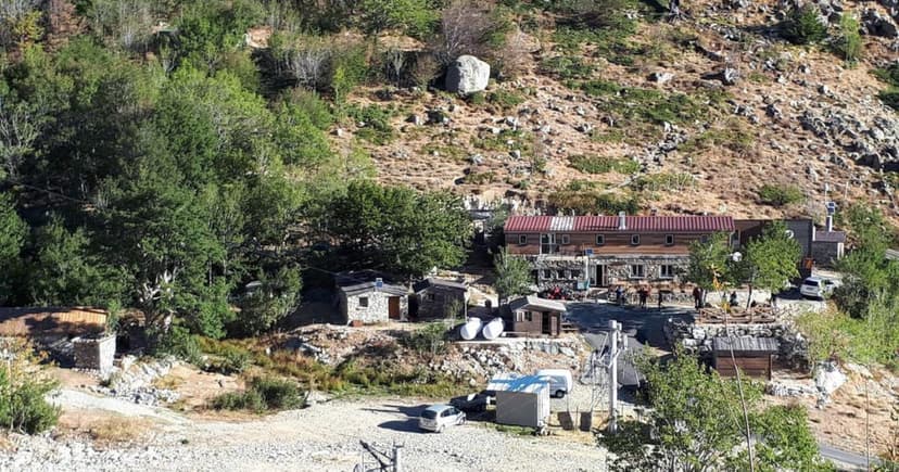 Mountain refuge buildings at Bergeries de Capannelle nestled in a dry, rocky, and wooded hillside.