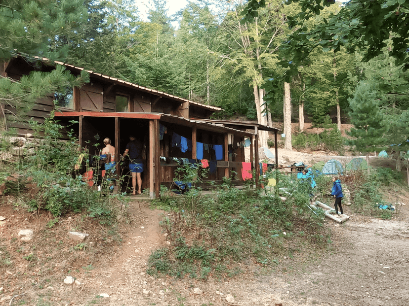 Wooden cabin in a dense forest with people outside and clothes drying on a line.
