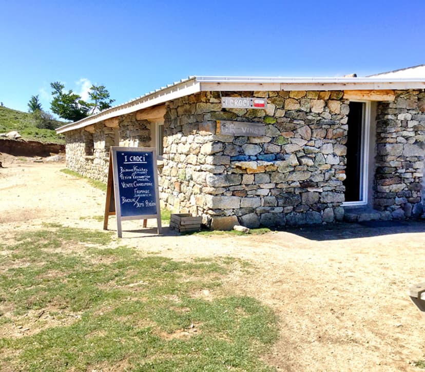 Stone building with chalkboard menu outside in a grassy, sunny mountain setting, labeled "I CROCI".