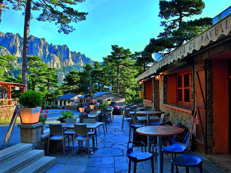 Outdoor cafe seating at Col de Bavella with rugged mountains and pine forest backdrop.
