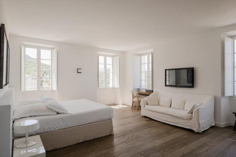 Bright bedroom with white linens, wood floor, and view of green hills in Corsica.
